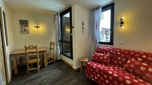 En kompakt opholdsstue med spiseplads, en sofa og et vindue med gardiner.