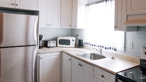 A kitchen with white cabinets, a stainless steel refrigerator, a microwave, and a sink.