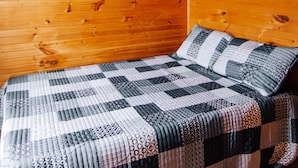 A wooden cabin room with a bed, a ceiling fan, and a window.