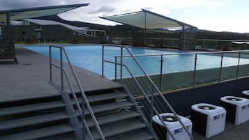 A swimming pool with steps leading down to the water, a stone building in the background, and a clear sky.