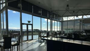 Ein modernes Restaurant mit großen Fenstern und Blick auf Wasser und Berge.