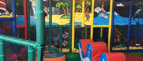 A children's play area with colorful play structures, including a slide, climbing net, and soft play surfaces.