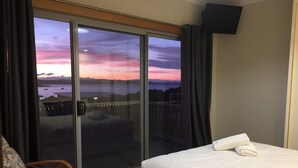 Ein Hotelzimmer mit Bett, Stuhl und einer Schiebetür zum Balkon mit Blick auf Meer und Berge.