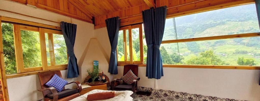 A room with a bed, two chairs, a window with curtains, and a view of greenery.