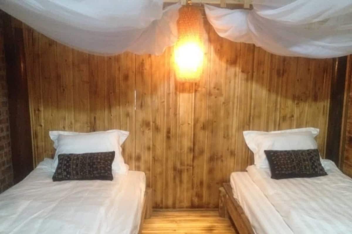 Quarto com duas camas, paredes de madeira e luminária central.