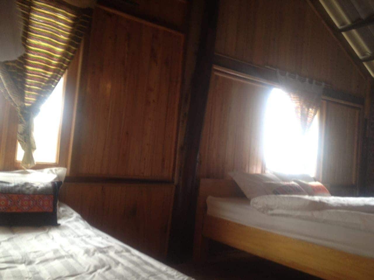 A wooden room with two beds, one with a patterned bedspread and the other with a plain one.