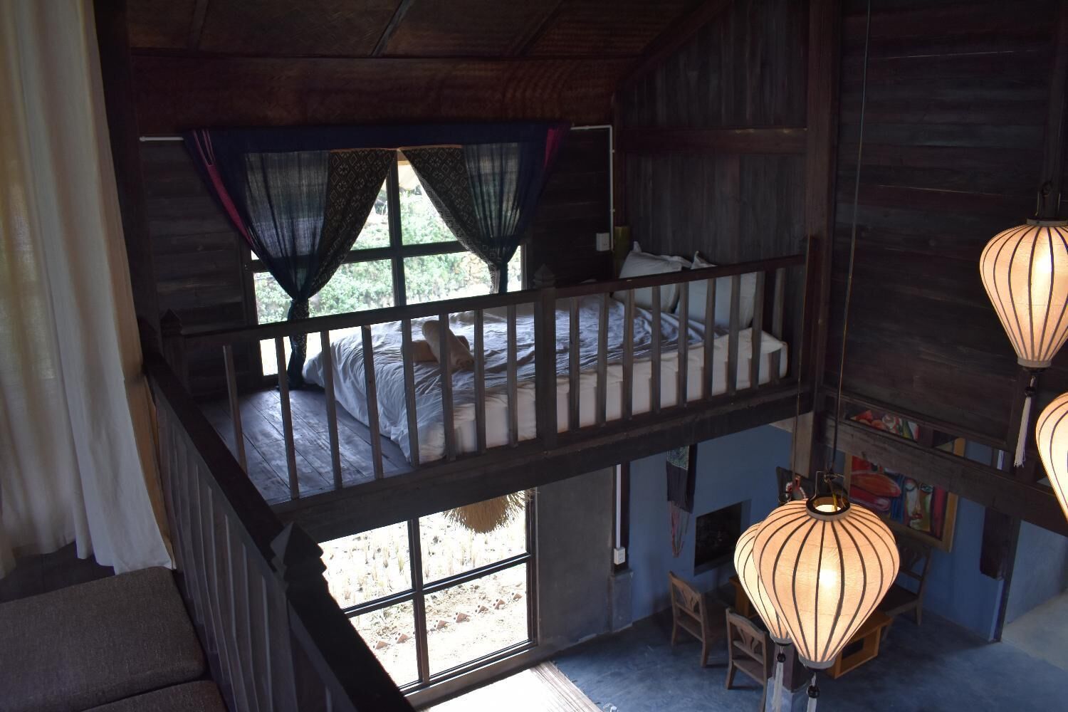 A rustic cabin with a loft bedroom, a balcony, and a dining area with hanging lanterns.