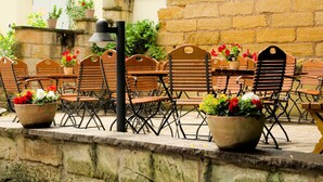 An outdoor seating area with wooden chairs and tables, potted plants, and a stone wall. - Double room large (with balcony/terrace) - Brauerei-Gasthof Pfister (Eggolsheim)