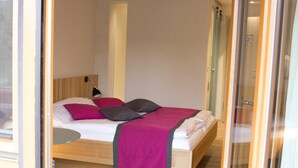 A modern bedroom with a wooden bed frame, a bedside table, and a nightstand. - Double room large (with balcony/terrace) - Brauerei-Gasthof Pfister (Eggolsheim)