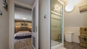 A bedroom with a bed, a glass shower enclosure, and a bathroom with a tiled floor and a wicker basket. - La Tronquiere (Lacropte)