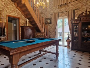 A pool table in a room with patterned wallpaper, a staircase, and a wooden cabinet.