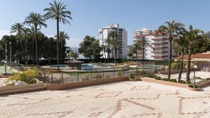 Une piscine sur le toit, agrémentée de palmiers, un terrain de basket et des bâtiments modernes en arrière-plan.