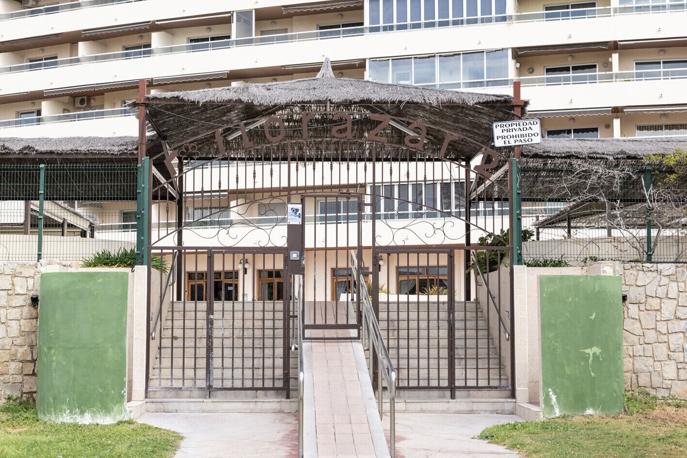 A gated entrance with a metal gate and a covered walkway leading to a building with multiple windows.