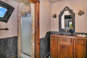 Un baño con un arco de piedra, un espejo grande con marco ornamentado y un tocador de madera con lavamanos.