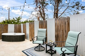 Un patio al aire libre con dos sillas verdes acolchadas, una mesita y un jacuzzi.