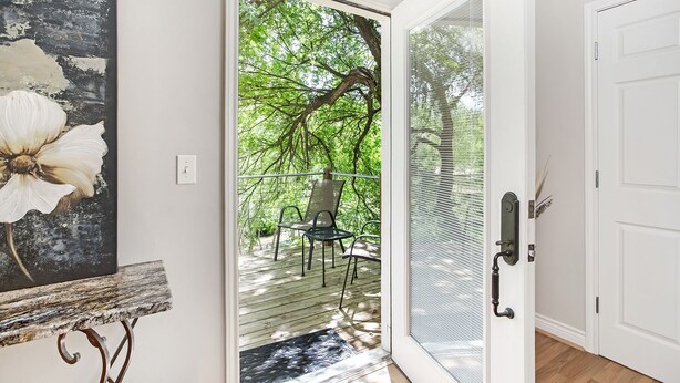 A room with a sliding glass door leading to an outdoor deck with chairs, a white door, and a framed artwork on the wall.