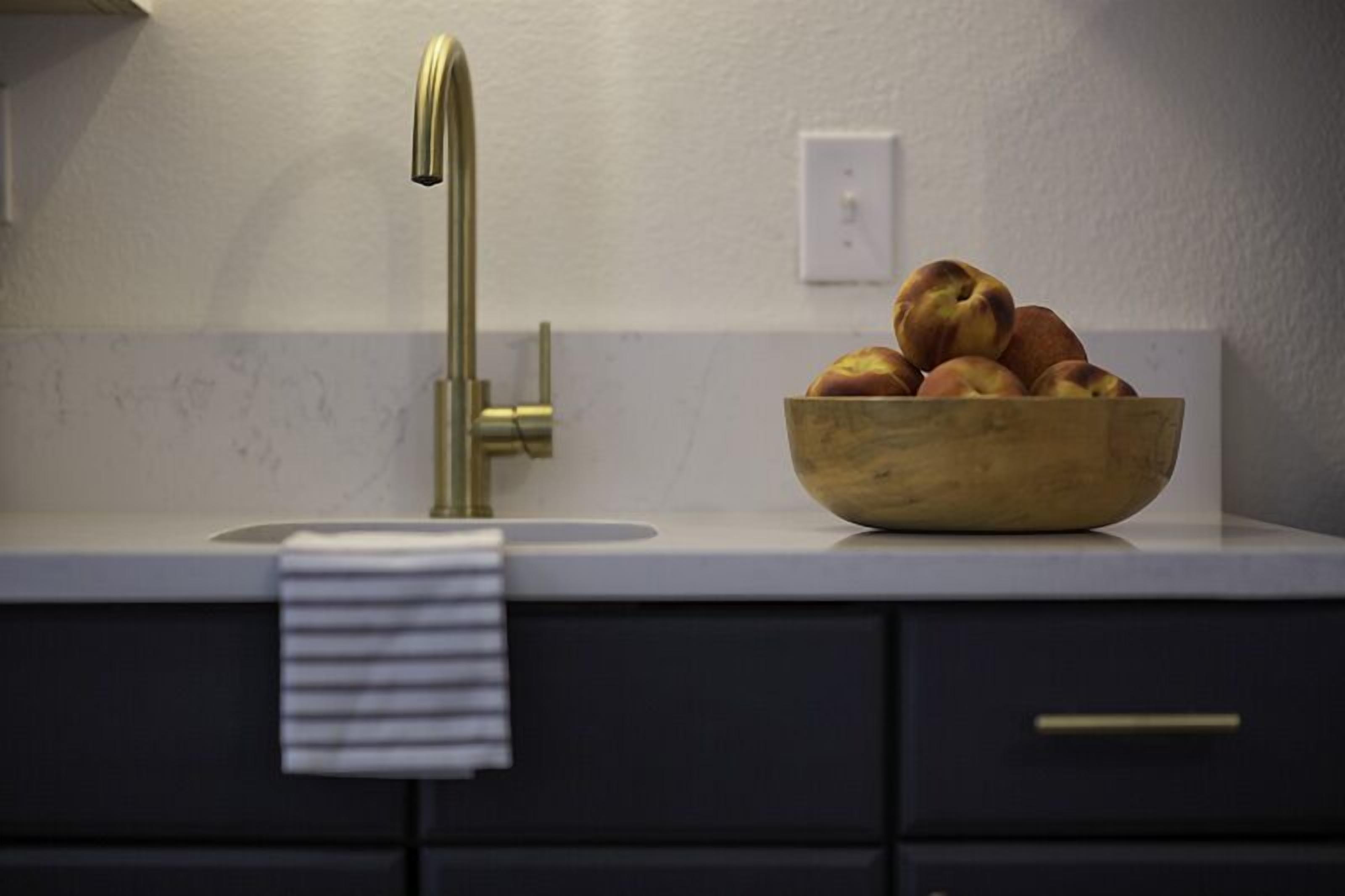 Una cocina con un tazón de madera lleno de fruta sobre la encimera, un grifo moderno y una toalla colgada en el lavabo.