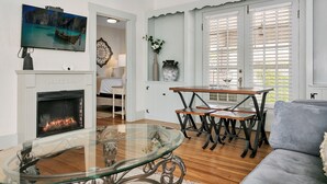 A living room with a fireplace, a glass coffee table, a sofa, and a dining area with a table and chairs.