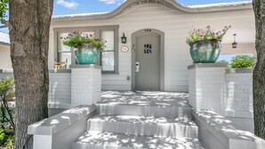 A house with a grey door, white brick steps, and two large flower pots on either side.