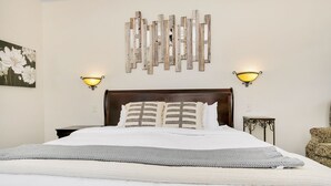 A neatly made bed with a grey knitted throw, a wooden headboard, and two wall-mounted lamps.
