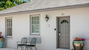 A house with a grey door, a sign reading "Hummingbird Hideaway," and two metal chairs outside.