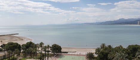 A coastal view with a beach, tennis courts, and palm trees.
