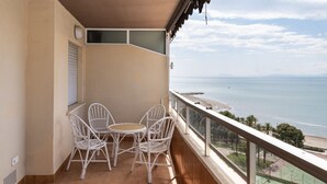 Un balcon avec des fauteuils en osier blanc et une petite table ronde, donnant sur une plage et un court de tennis.