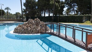Une piscine agrémentée d’un élément rocheux, entourée de palmiers et dotée d’une terrasse en bois.
