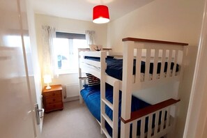 Une chambre avec des lits superposés, une table de chevet, une lampe et une fenêtre avec des rideaux.