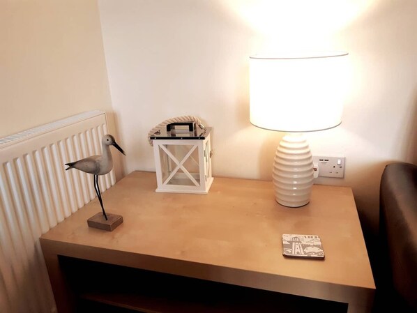 A bedside table with a lamp, a decorative bird, a lantern, and a coaster.