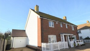 Une maison à deux étages, construite en briques, avec une porte de garage blanche, une clôture en bois peinte en blanc et un petit porche agrémenté de plantes en pot.