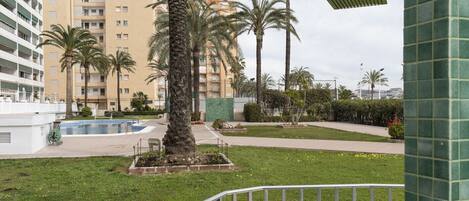 A residential building with a swimming pool, palm trees, and a well-maintained lawn.