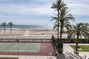 A beach view with palm trees, a tennis court, and a sandy beach.