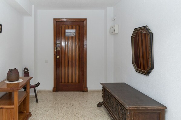 A hallway with a wooden door, a small table with a vase, a bench, and a mirror on the wall.