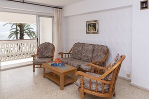 Un salon comprenant un canapé, deux fauteuils, une table basse et un balcon offrant une vue sur les palmiers.