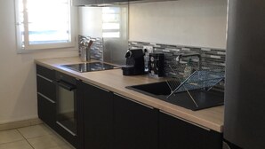 Une cuisine moderne avec des meubles de couleur sombre, un réfrigérateur en acier inoxydable, une machine à café et une fenêtre équipée de stores.