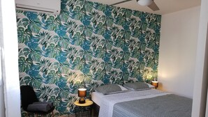 Une chambre à coucher avec un lit, deux lampes de chevet, une chaise et un mur orné d’un motif de feuilles tropicales.