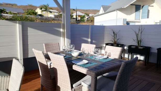 Une terrasse extérieure avec une table dressée pour le repas, entourée de chaises en osier et de plantes en pot.