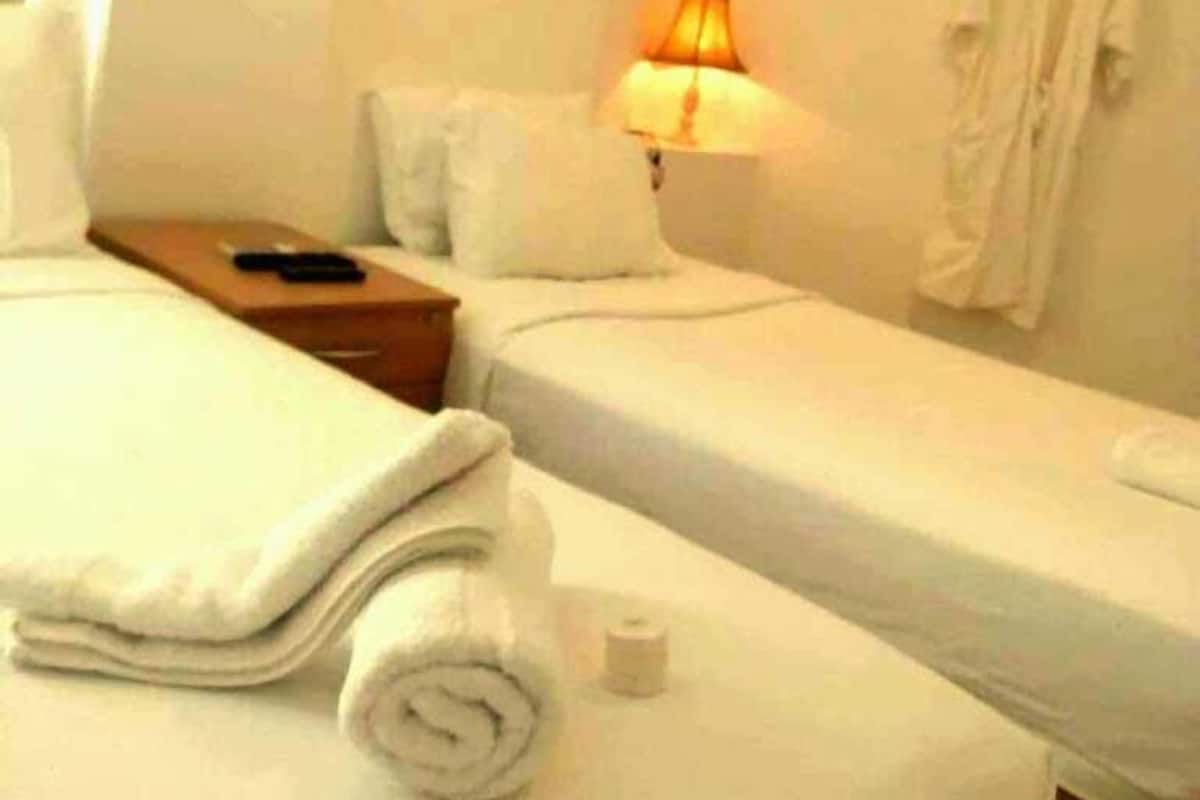 Une chambre d’hôtel avec deux lits simples, une table de chevet avec une lampe et un peignoir accroché au mur.