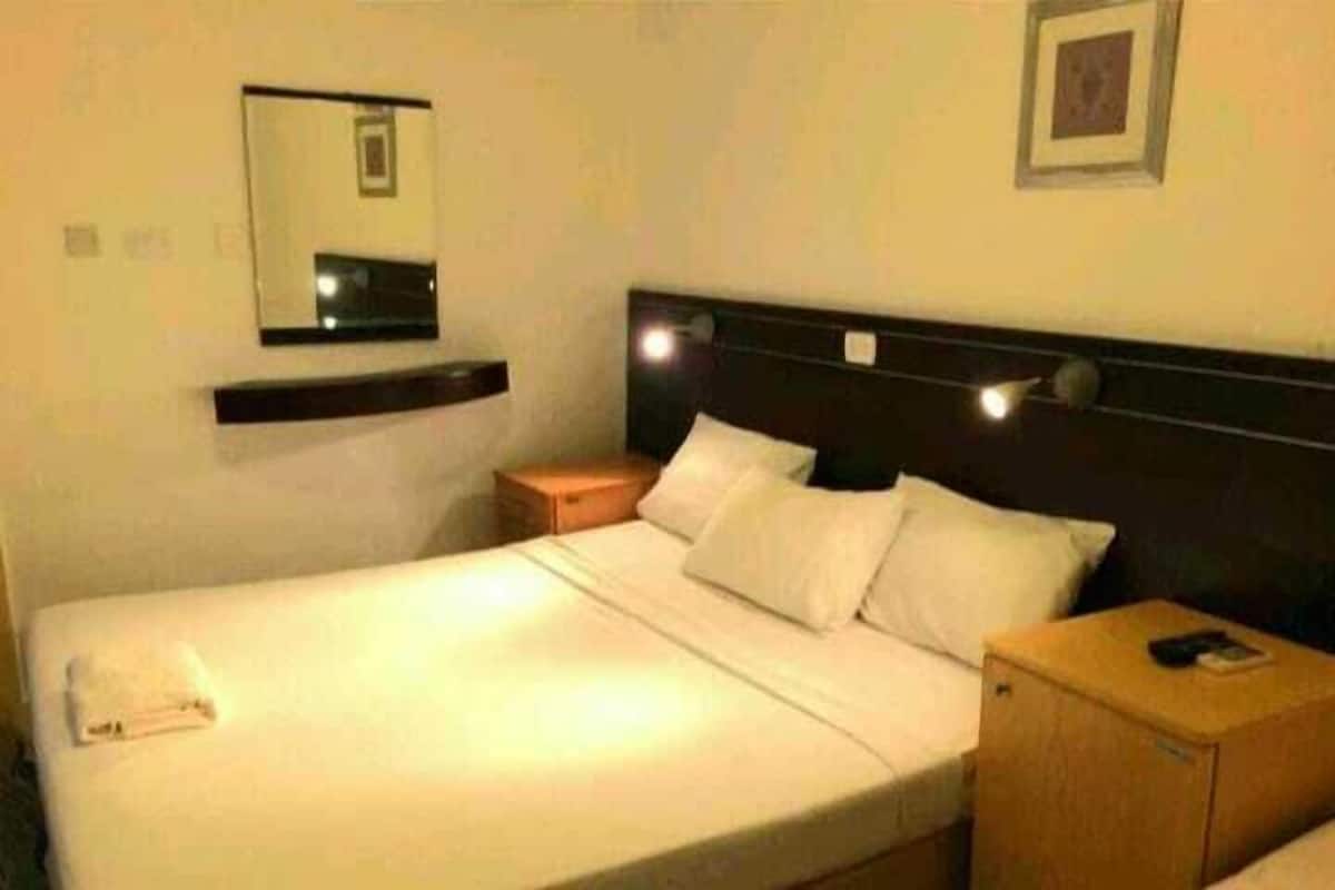 Une chambre d’hôtel avec un lit simple, une table de chevet, une commode, un miroir et un tableau encadré au mur.