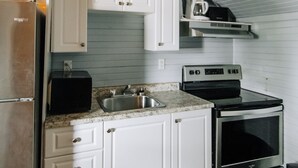 A compact kitchen with white cabinets, a stainless steel refrigerator, a stove, and a coffee maker on a shelf. - BEACHFRONT COTTAGE IN WASAGA BEACH - SANDPIPER BEACH RESORT - COTTAGE # 8 (Wasaga Beach)
