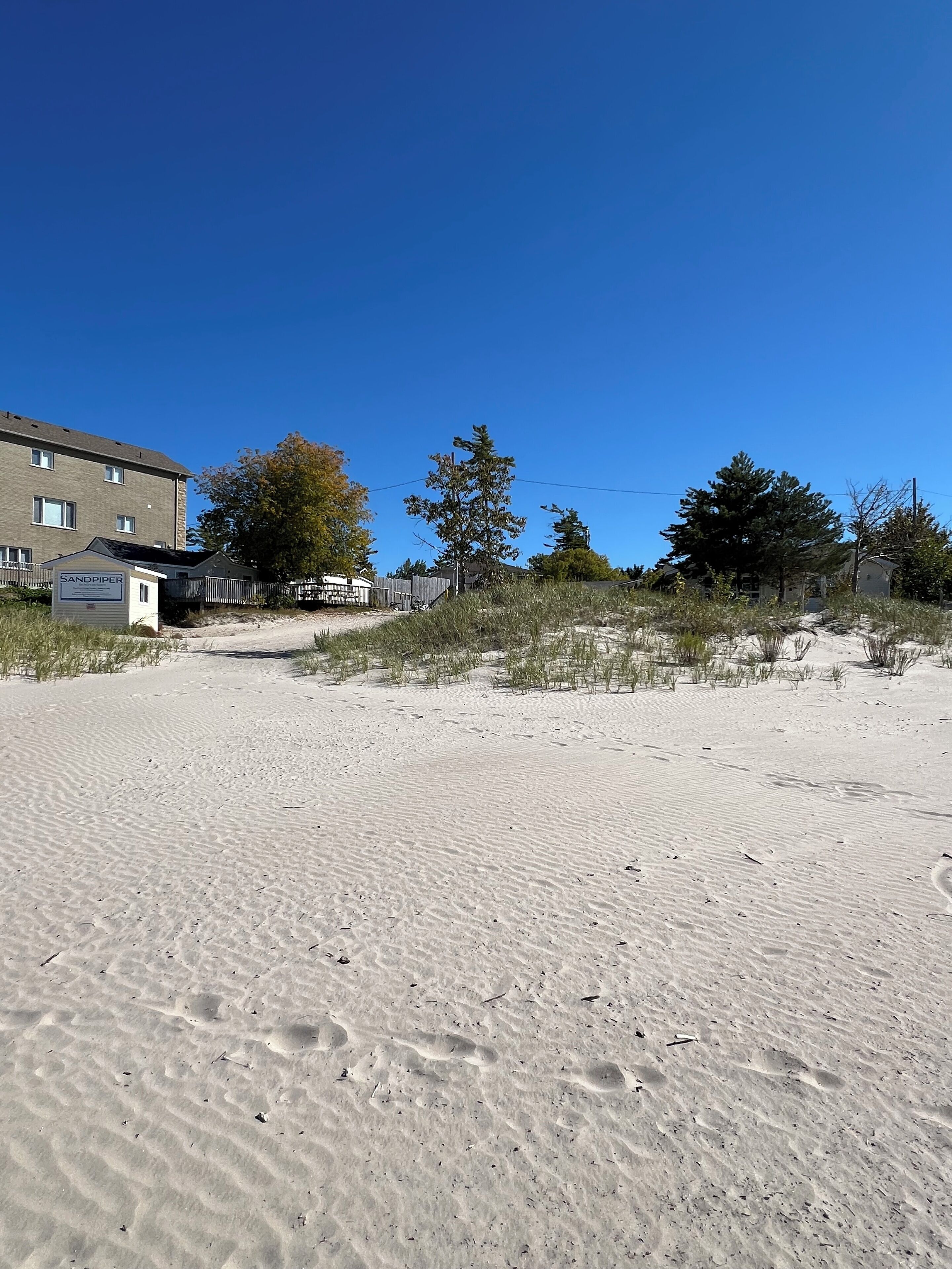 A sandy beach with footprints, a sign for Sandpiper, and a building in the background.