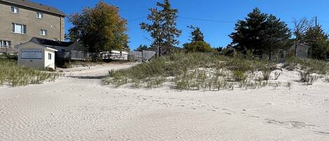 A sandy beach with footprints, a sign for Sandpiper, and a building in the background.