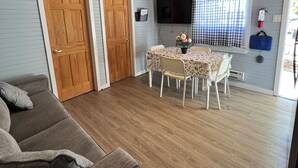 A cozy room with a wooden ceiling, a dining table with chairs, a grey sofa, and two wooden doors. - BEACHFRONT COTTAGE IN WASAGA BEACH - SANDPIPER BEACH RESORT - COTTAGE # 8 (Wasaga Beach)