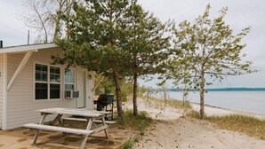 Un chalet situé au bord de la plage, équipé d’une table de pique-nique et d’un barbecue, entouré d’arbres et offrant une vue sur l’eau.