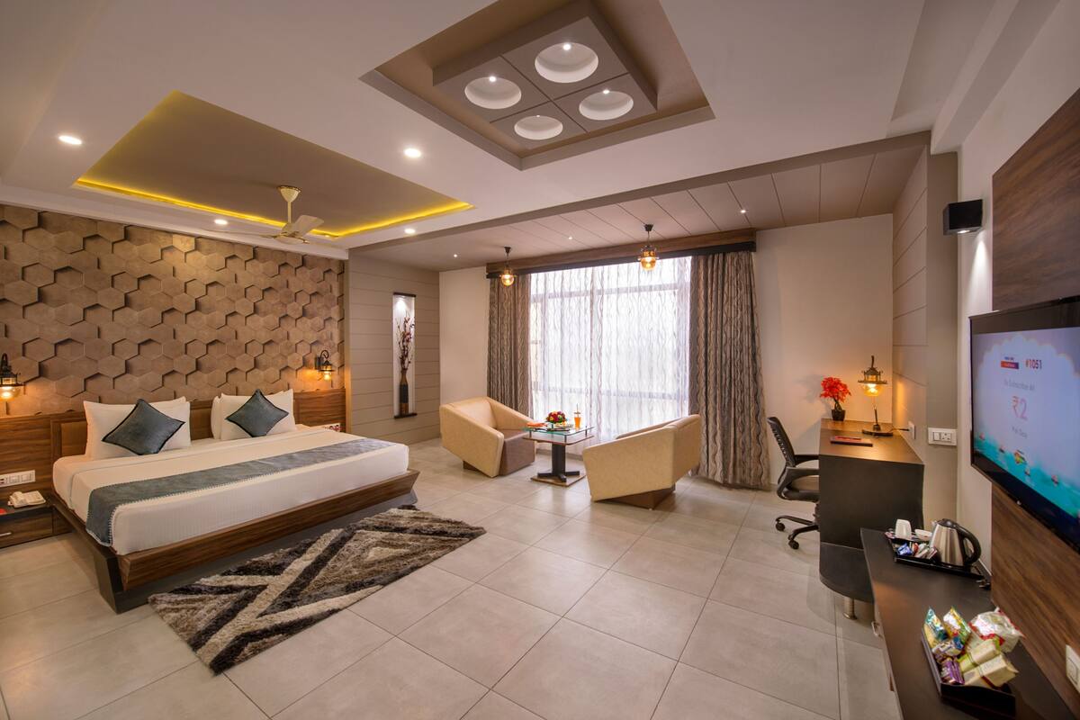 Quarto de hotel moderno com uma cama grande, uma mesa de trabalho, uma televisão e um espaço de estar.