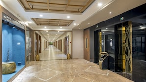 A long, well-lit corridor with marble flooring, directional signs, and a modern elevator area.