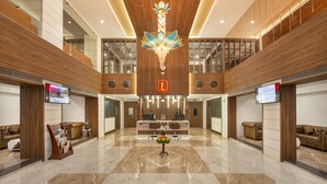 A spacious lobby with a central reception desk, wooden paneling, and a chandelier.