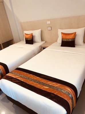 Two single beds with white bedding and decorative pillows, a wooden headboard, and a bedside table.