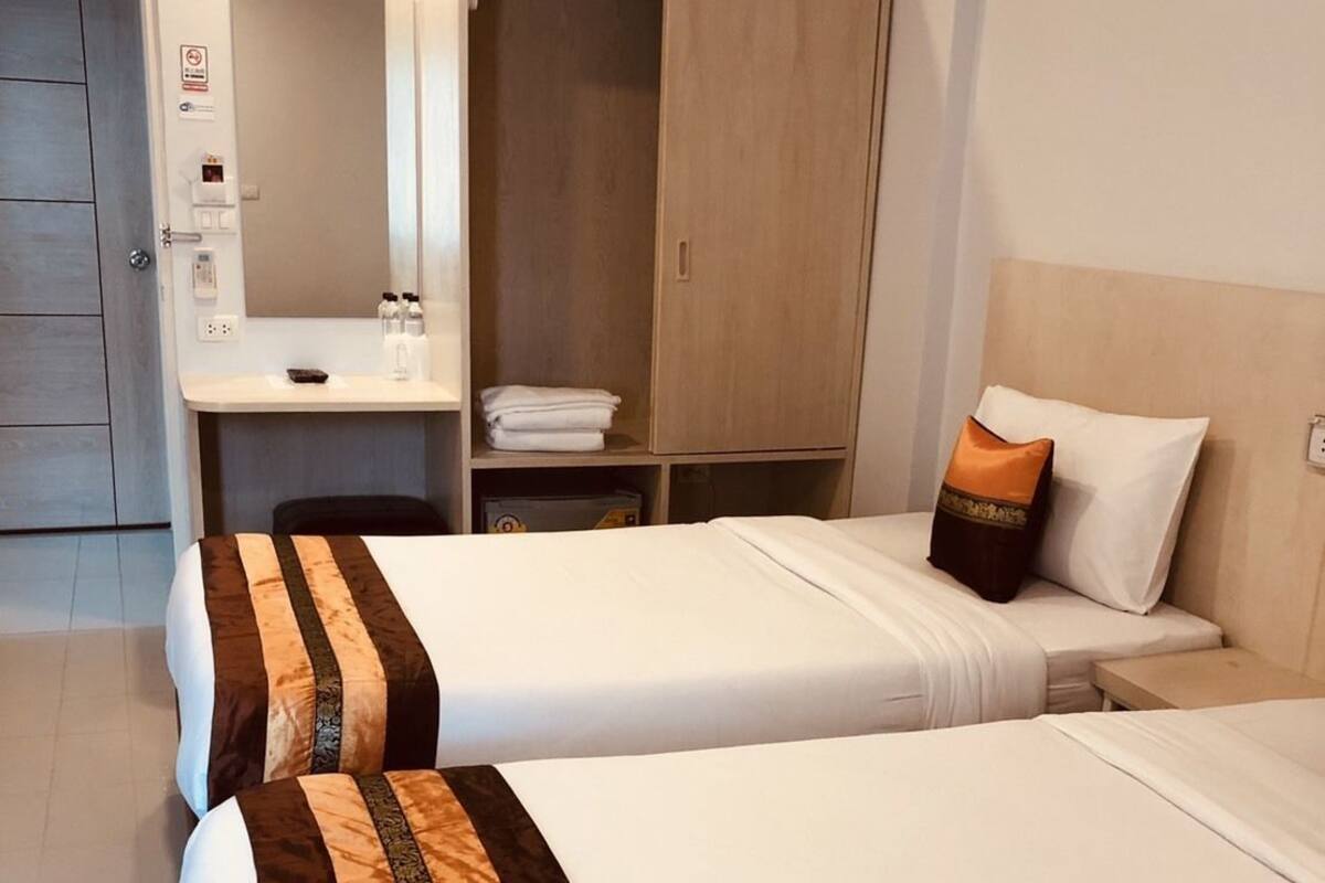 A hotel room with two beds, a desk, a wardrobe, and a mirror.